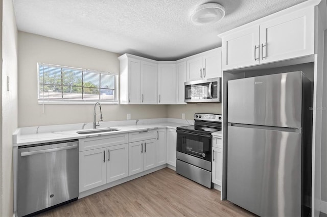 kitchen featuring a sink, a textured ceiling, white cabinetry, stainless steel appliances, and light wood-style flooring