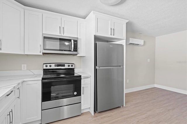 kitchen featuring a wall mounted AC, baseboards, white cabinets, light wood-style floors, and stainless steel appliances
