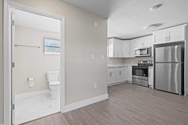 kitchen featuring white cabinets, baseboards, light countertops, a textured ceiling, and stainless steel appliances