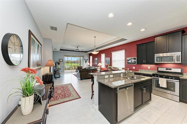 kitchen featuring an island with sink, stainless steel appliances, sink, light stone countertops, and decorative light fixtures