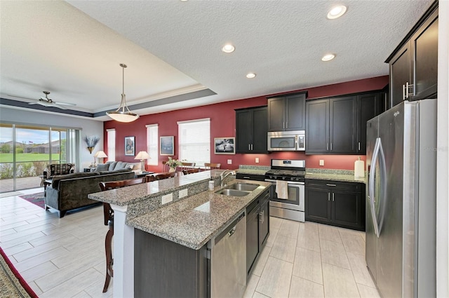 kitchen with hanging light fixtures, ceiling fan, appliances with stainless steel finishes, an island with sink, and sink