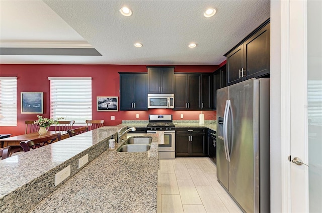 kitchen with sink, appliances with stainless steel finishes, light stone counters, and a textured ceiling