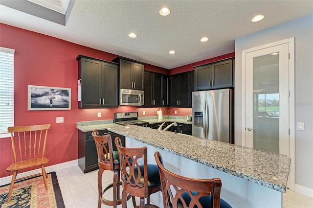 kitchen with a textured ceiling, light stone countertops, stainless steel appliances, and a healthy amount of sunlight