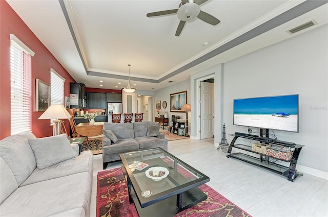 living room with ornamental molding, light tile patterned floors, a raised ceiling, and ceiling fan