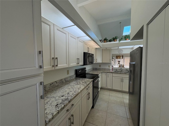 kitchen with black appliances, light stone counters, a sink, a skylight, and light tile patterned floors