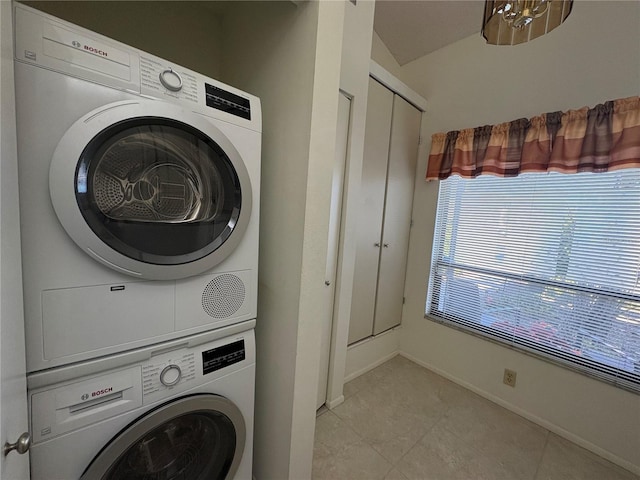 clothes washing area with light tile patterned floors, baseboards, laundry area, and stacked washing maching and dryer