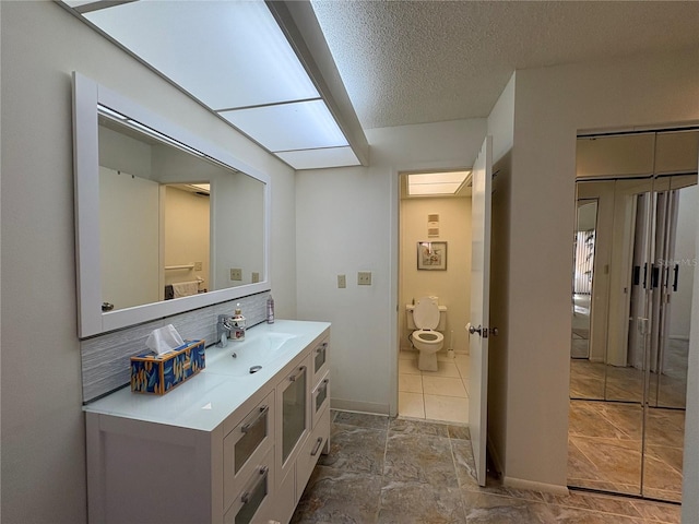 bathroom featuring tasteful backsplash, baseboards, toilet, vanity, and a textured ceiling