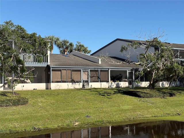 rear view of property featuring roof mounted solar panels, a water view, a yard, and a sunroom