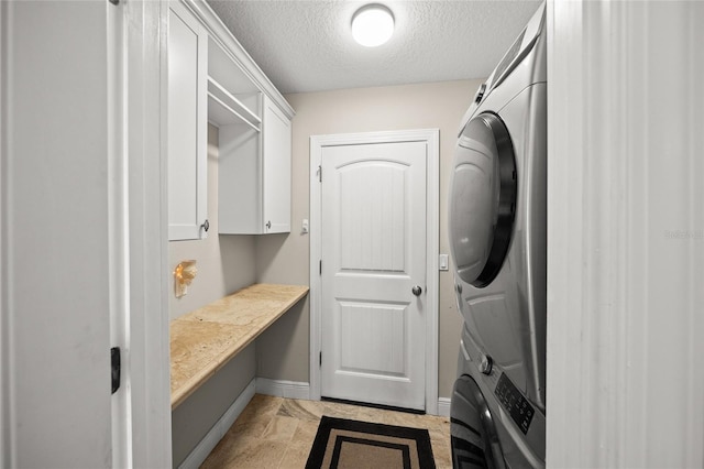 laundry room with a textured ceiling, cabinets, and stacked washer / drying machine