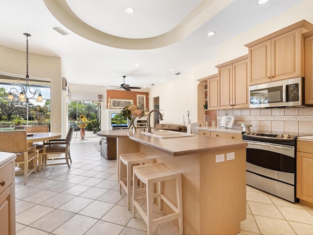 kitchen featuring stainless steel appliances, light tile patterned flooring, ceiling fan with notable chandelier, and a kitchen island with sink