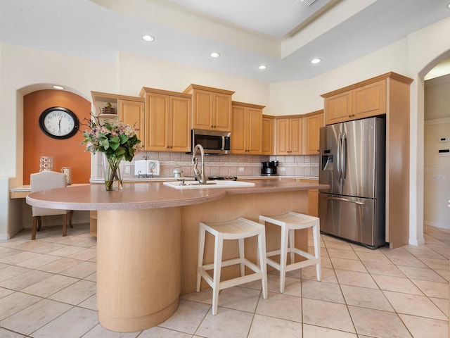 kitchen featuring decorative backsplash, a kitchen island with sink, a kitchen breakfast bar, light tile patterned floors, and appliances with stainless steel finishes