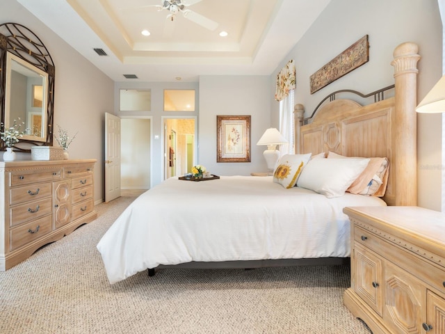 bedroom featuring ensuite bath, a raised ceiling, light carpet, and ceiling fan