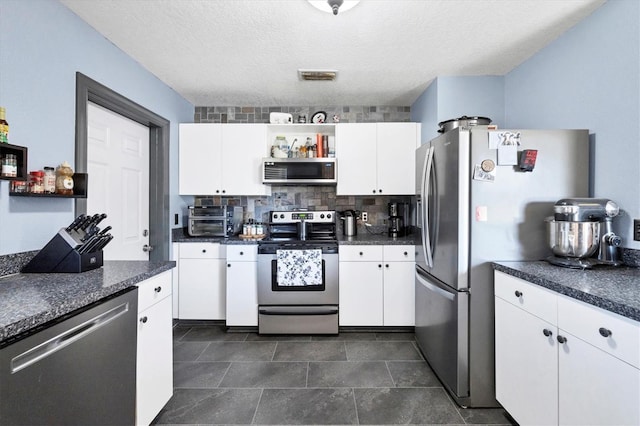 kitchen featuring decorative backsplash, white cabinets, appliances with stainless steel finishes, a textured ceiling, and dark tile patterned flooring