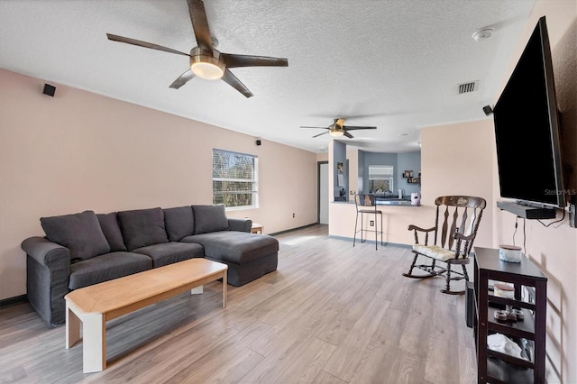 living room with a textured ceiling, light wood-type flooring, and ceiling fan