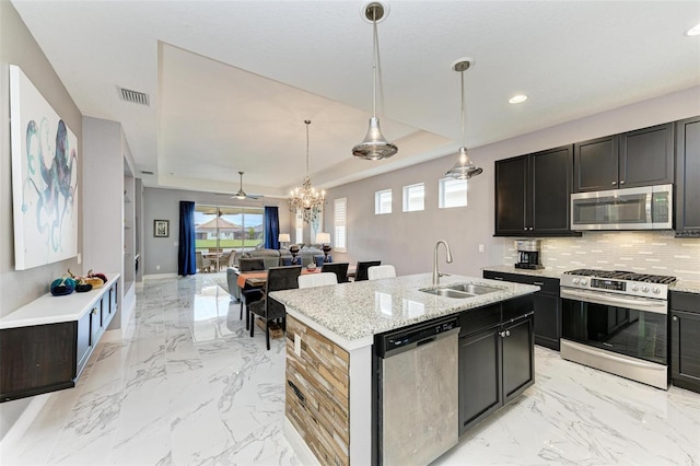 kitchen featuring appliances with stainless steel finishes, sink, pendant lighting, light stone counters, and a kitchen island with sink