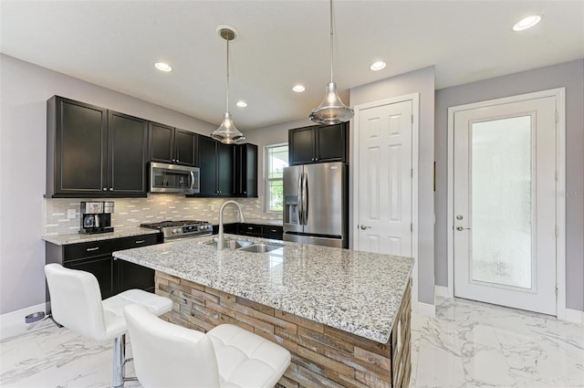 kitchen featuring light stone countertops, appliances with stainless steel finishes, sink, decorative light fixtures, and a center island with sink