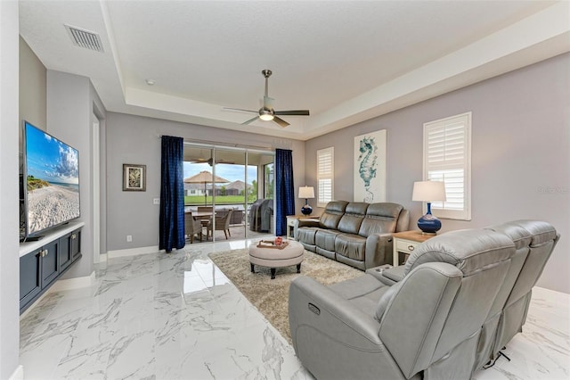 living room with a tray ceiling, a healthy amount of sunlight, and ceiling fan