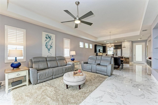 living room with a healthy amount of sunlight, a tray ceiling, and ceiling fan with notable chandelier