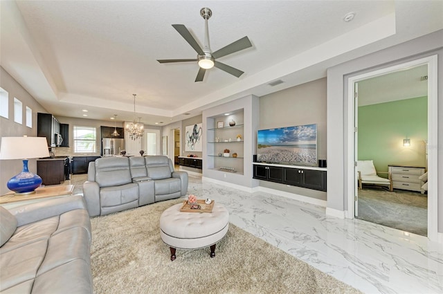 living room with a textured ceiling, a tray ceiling, ceiling fan with notable chandelier, and built in shelves