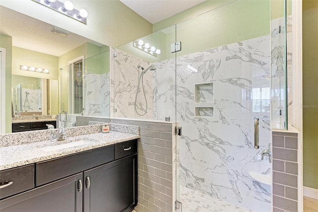 bathroom with a shower with door, a textured ceiling, vanity, and tile walls