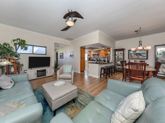 living room featuring ornamental molding, light wood-type flooring, and ceiling fan with notable chandelier