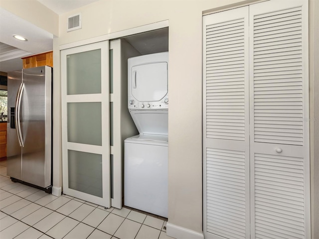 clothes washing area featuring light tile patterned floors and stacked washing maching and dryer