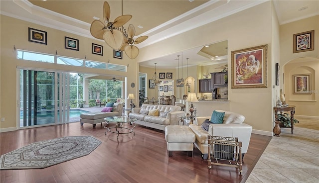 living room with ceiling fan, a raised ceiling, a towering ceiling, light hardwood / wood-style floors, and ornamental molding