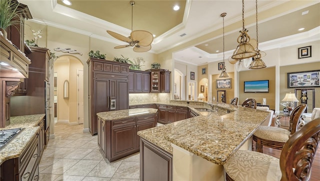 kitchen with kitchen peninsula, a tray ceiling, ceiling fan, and a breakfast bar area