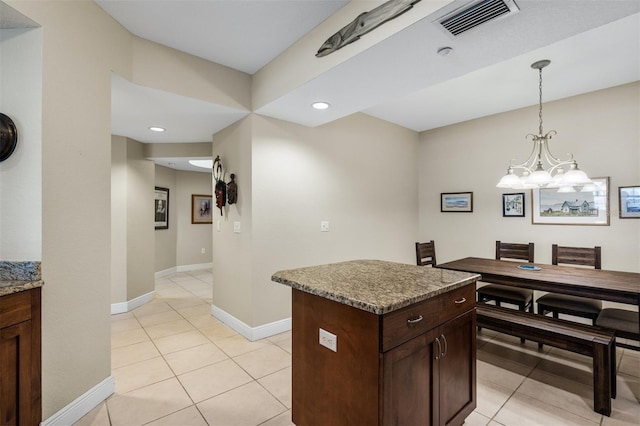 kitchen with light tile patterned floors, a kitchen island, light stone countertops, a notable chandelier, and dark brown cabinetry