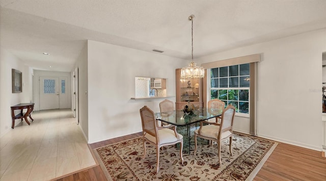 dining room featuring an inviting chandelier, light hardwood / wood-style flooring, and a textured ceiling