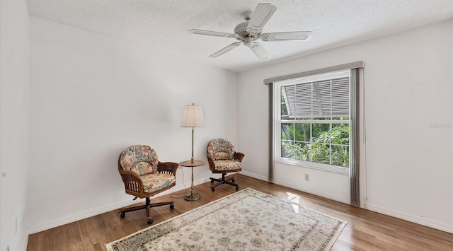 living area featuring a textured ceiling, light wood-type flooring, and ceiling fan