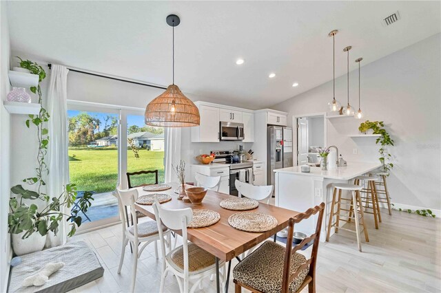 dining area with light hardwood / wood-style flooring, sink, and vaulted ceiling