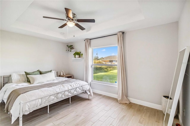 bedroom with a tray ceiling, light wood-type flooring, and ceiling fan