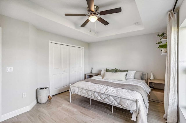 bedroom with light hardwood / wood-style floors, a tray ceiling, a closet, and ceiling fan