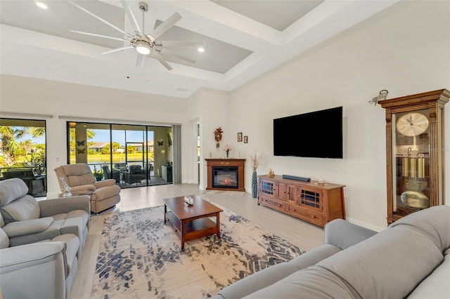 living room with a towering ceiling, light hardwood / wood-style flooring, beamed ceiling, and ceiling fan