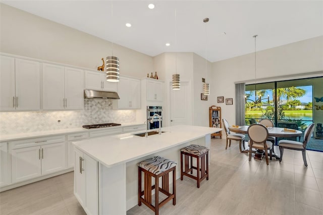 kitchen with white cabinets, stainless steel appliances, pendant lighting, and a kitchen island with sink