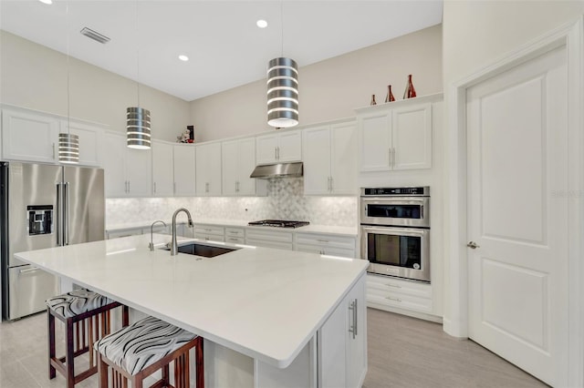 kitchen with sink, an island with sink, hanging light fixtures, and stainless steel appliances