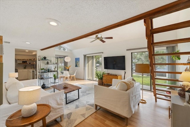 living room with a textured ceiling, lofted ceiling with beams, light wood-type flooring, and ceiling fan