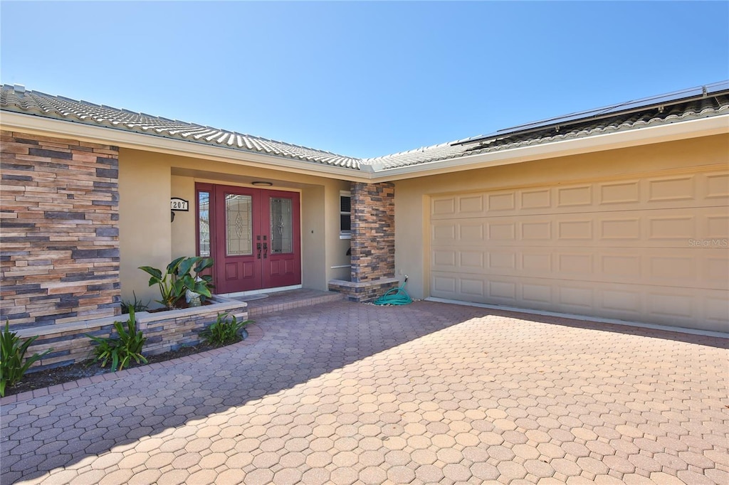 7207 13th Ave W, Bradenton, FL 34209 - property entrance with stucco siding, a tiled roof, decorative driveway, a garage, and french doors