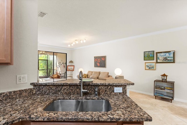 kitchen featuring dark stone counters, kitchen peninsula, sink, and ornamental molding