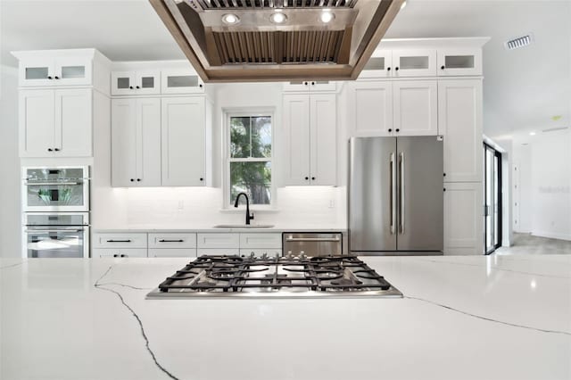 kitchen with appliances with stainless steel finishes, light stone counters, custom range hood, sink, and white cabinetry