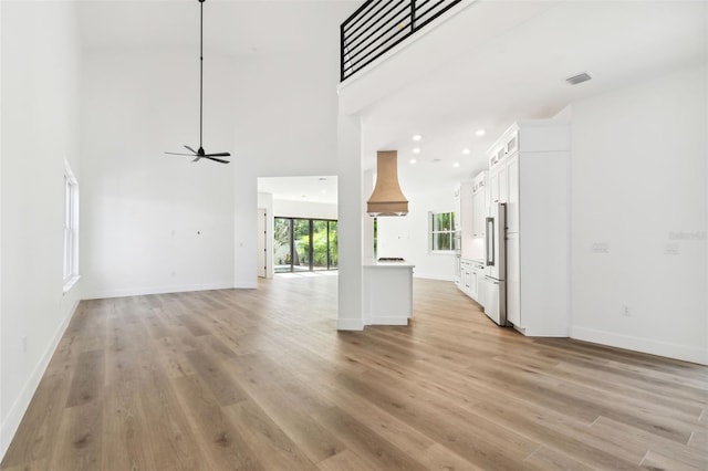 unfurnished living room with ceiling fan, light wood-type flooring, and a towering ceiling