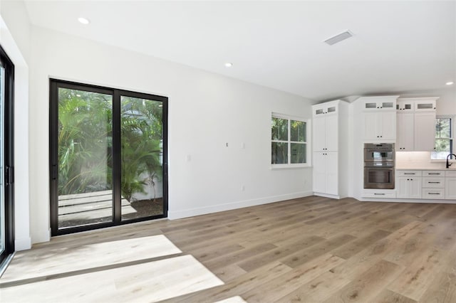 unfurnished living room featuring a wealth of natural light, light hardwood / wood-style flooring, and sink