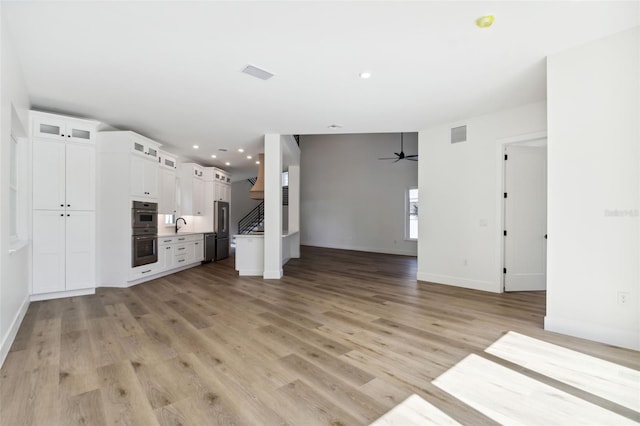 unfurnished living room featuring ceiling fan, sink, and light wood-type flooring