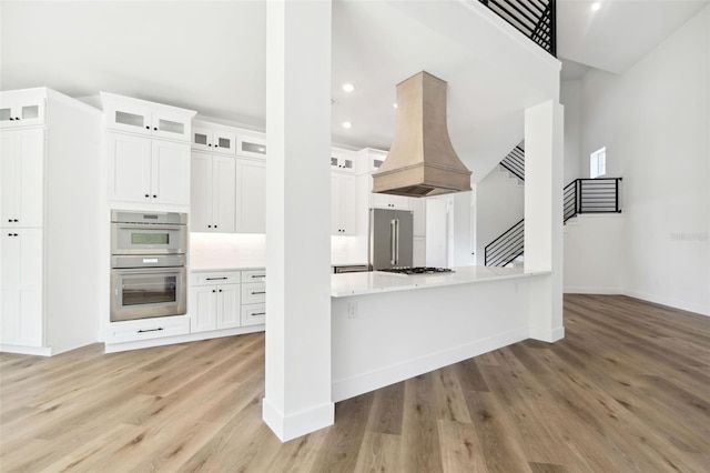 kitchen featuring white cabinets, appliances with stainless steel finishes, light hardwood / wood-style flooring, and custom exhaust hood