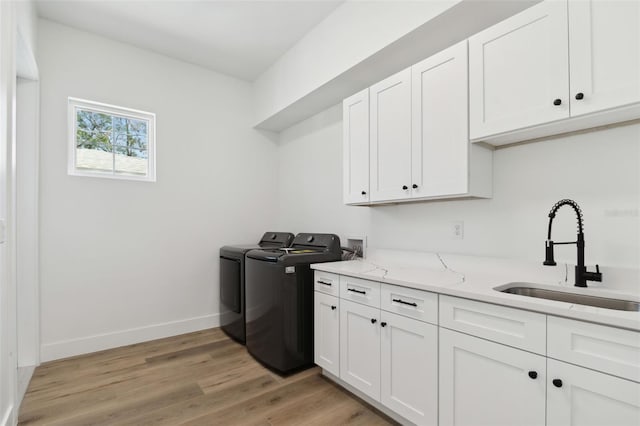 clothes washing area featuring washer and clothes dryer, cabinets, light wood-type flooring, and sink