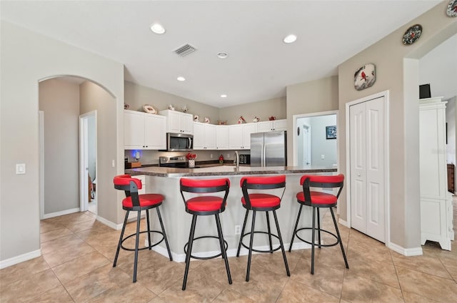 kitchen with a center island with sink, a breakfast bar, light tile patterned flooring, white cabinetry, and appliances with stainless steel finishes