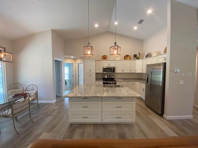 kitchen with white cabinetry, stainless steel appliances, light hardwood / wood-style floors, and an island with sink