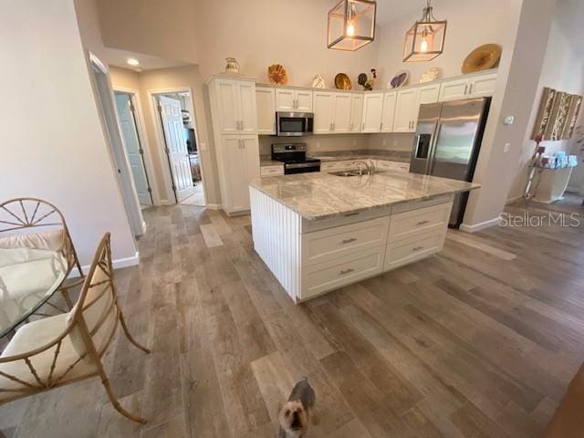 kitchen featuring white cabinetry, stainless steel appliances, decorative light fixtures, and a kitchen island with sink