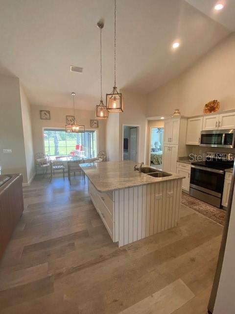 kitchen featuring an island with sink, white cabinetry, hardwood / wood-style flooring, sink, and stainless steel appliances